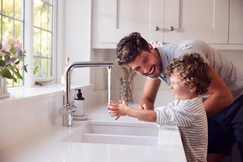 Child washing hands with warm running water at a sink.